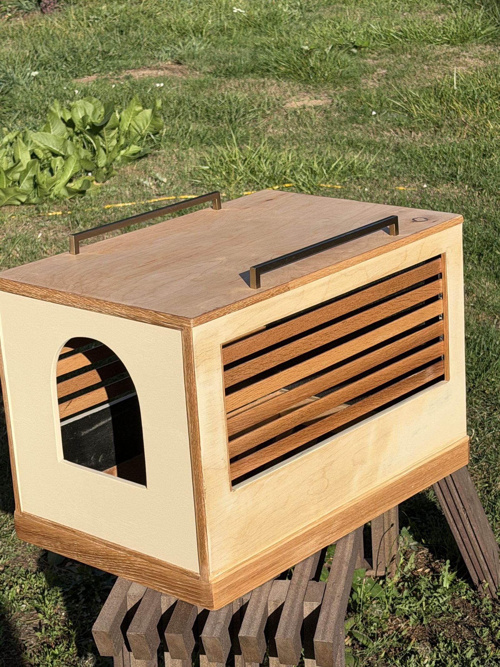 Cat box enclosure in birch with an arched entry, slatted side, and two bronze bar pulls on top