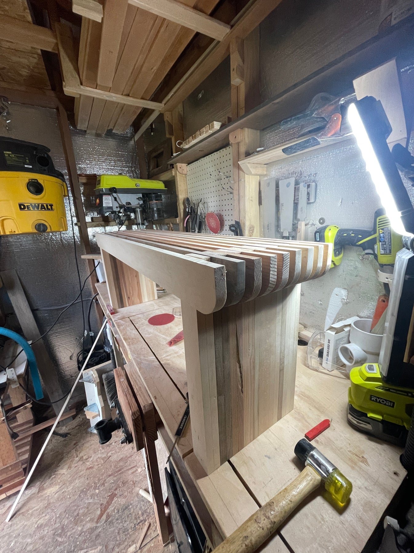 A slatted bench standing on the workbench mid-build, raking light across the slats